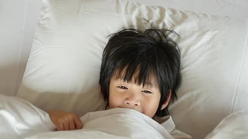 Linda criança asiática brincando de esconde-esconde na cama branca Câmera lenta