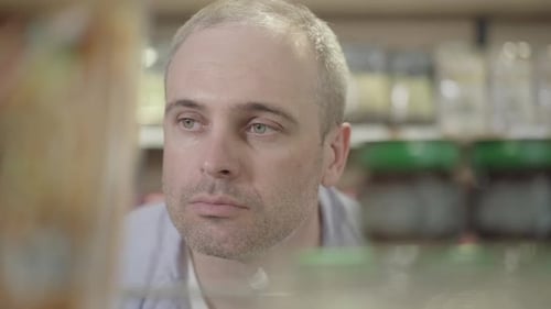 Close-up Face of Focused Confident Man Looking at Canned Food on Shelf. Portrait of Focused