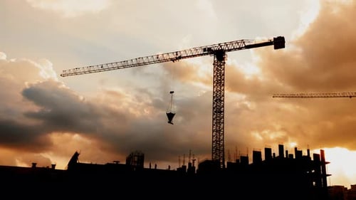 Silhouette of Tower Cranes Working on Construction Site Residential Golden Hour, Warm Cloudy Sky