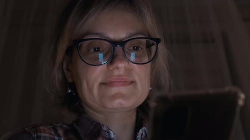 Woman Using Smartphone in Dark, Light Reflecting in Glasses