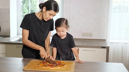 Mamá corta pizza recién horneada delante de su hija pequeña