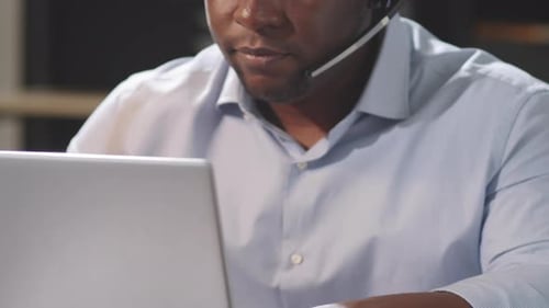 Black Male Call Center Agent Talking on Web Call and Typing on Laptop