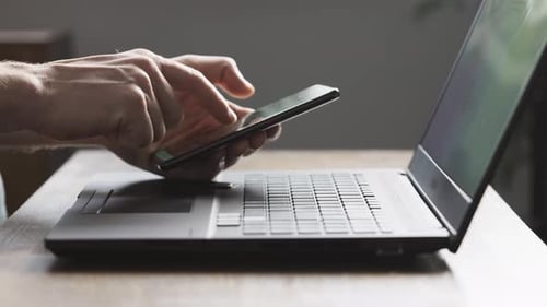 Man Using Smartphone and Laptop Connected to Work and Searching Information at Office