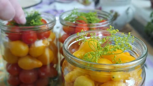 Housewife Puts Green Dill in Glass Jar with Yellow Tomatoes
