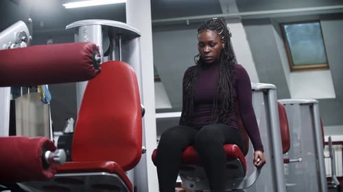 Uma mulher afro-americana malhando em uma academia em um equipamento de exercícios bombeando os músculos das pernas