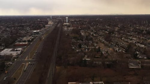 An aerial view of an empty railroad tracks. Residential homes are on the right, a highway, businesse