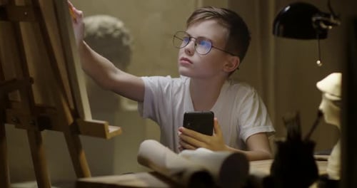 Boy Draws on Easel Using Smartphone for Reference