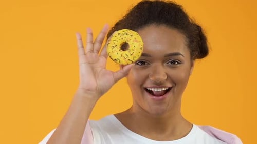 Cheerful Young Woman Holds Donut to Her Eye