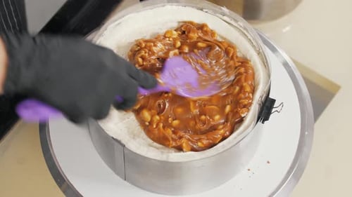 Konditor schmiert Karamell mit Erdnüssen über Vanillecreme