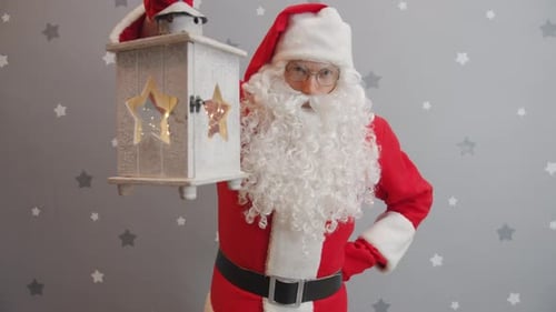 Portrait of Santa Claus Raising Lantern and Looking at Camera on Grey Background