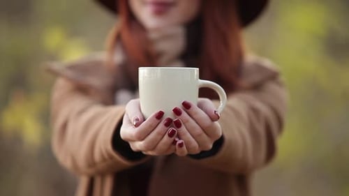 Redhead girl in yellow hat and coat with scarf and cup of coffee on autumn park