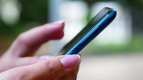 A woman is sitting in a cafe with a smartphone in her hands with a green screen mockup.