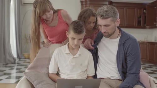 The Father and the Son Sitting Together on the Armchair with the Laptop. Beautiful Mother and