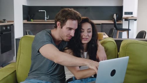 Smiling Couple Using Laptop Together on Couch at Home