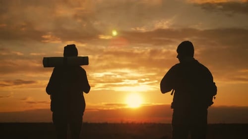 Silhouettes of Two Hikers with Backpacks Enjoying Sunset View From Top of a Mountain. Enjoying the