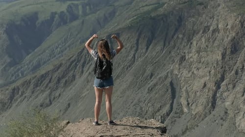 A Successful Woman Stands on a Cliff of a Mountain and Raises Her Hands Up. The Path To Success and