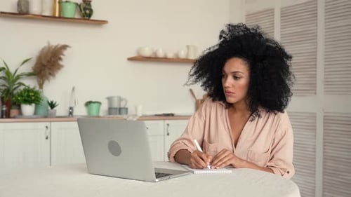 Young Woman Uses Laptop and Takes Notes at Home