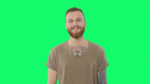 Glücklicher gutaussehender Mann auf Chroma Key. Positive bärtige tätowierte Hipster schaut in die Kamera und