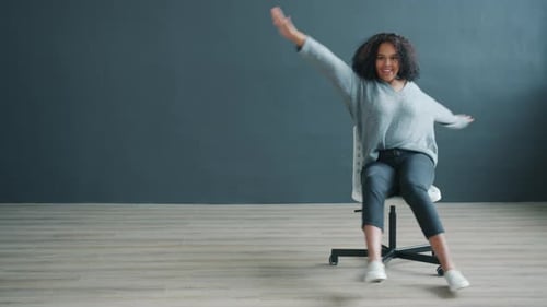 Cheerful Afro-American Woman Spinning on Office Chair Laughing Having Fun Indoors