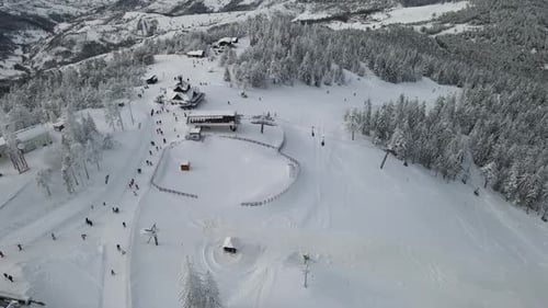 Top of mountain with ski lifts and people skiing. Beautiful panoramic aerial shot. Trees covered wit