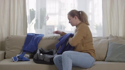 Young Sportswoman Putting Sportswear into Bag at Home