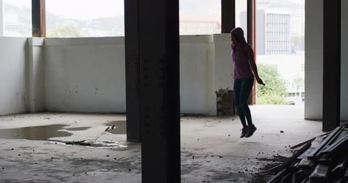 African american woman wearing hoodie skipping with rope in an empty urban building