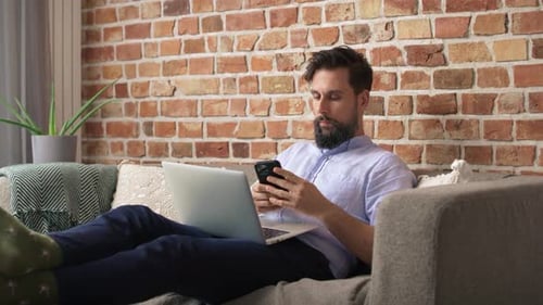 Man Relaxing on Couch with Laptop and Phone