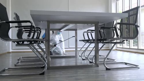 Worker in PPE suit cleaning in building with spray disinfectant water to remove covid 19