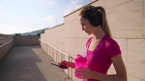 Young Woman is Resting After Morning Workout in Street Checking Message in Smartphone