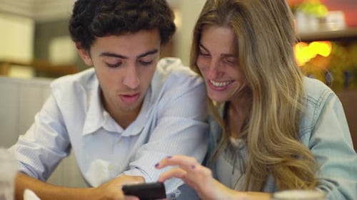 Friends Laughing, Looking at Smartphone in Restaurant