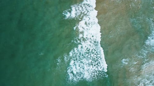 Aerial view of white sand beach and ocean wave. Zoom out.