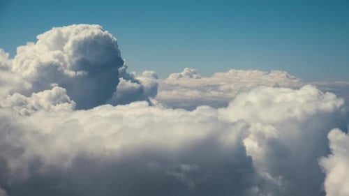Aerial view from airplane window of white puffy clouds on bright sunny day.