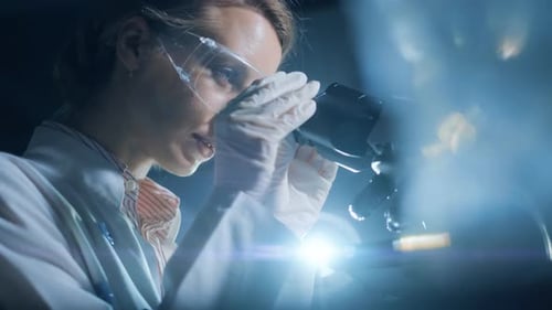Female Scientist Using Microscope in Dark Lab