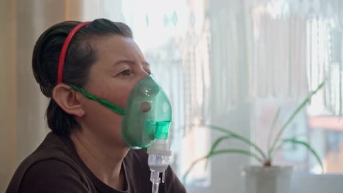 Une femme européenne à la maison effectue une inhalation de vapeurs d'huile oxygène à travers un masque
