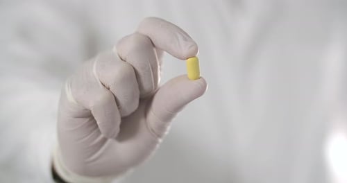 Gloved Hand Holding Yellow Medicine Capsule