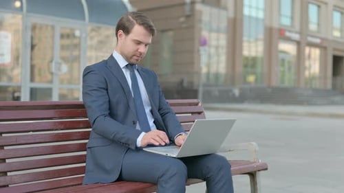 Man Celebrates While Using Laptop on Bench