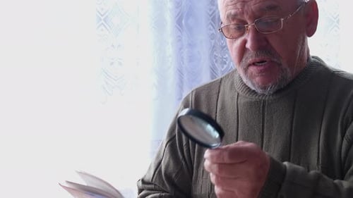 Senior Man Reads a Book with Magnifying Glass