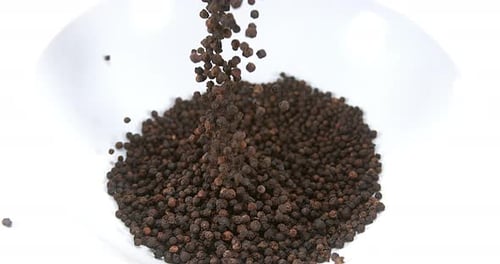 Black Peppercorns Pouring into a White Bowl