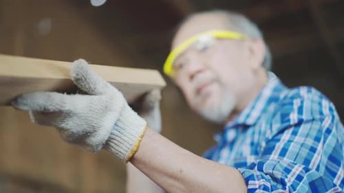 Asian senior male carpenter equals a wooden bar in the workshop