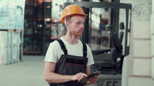 Man in Uniform with Cipboard Is Standing in the Storehouse
