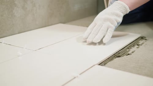 Worker laying white floor tiles at home