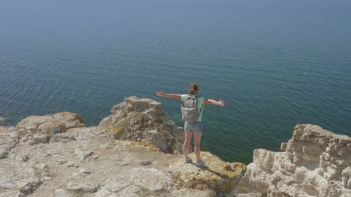 Aerial flyby with drone woman traveler standing on rocky shore sea