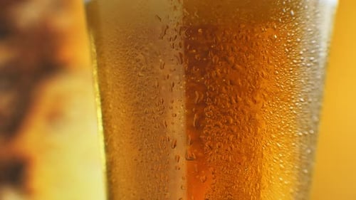 Macro tiro de burbujas finas que se elevan en un vaso con líquido naranja. Cerveza fría en un vaso con