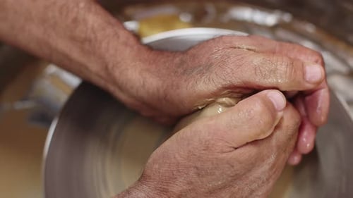 Les mains des potiers tiennent un morceau d'argile tournant sur une roue de potier lui donnant une forme vue de dessus en gros plan