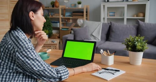 Young Woman Looking at Green Mock-up Laptop Screen Watching Media at Home