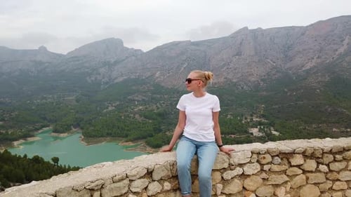 Woman Sitting and Looking at a Beautiful View with a Blue Lake and Mountains From the Wall
