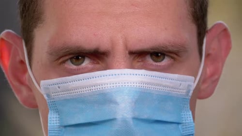 Young Man in a Medical Protective Face Mask Looking at the Camera on the Street Background