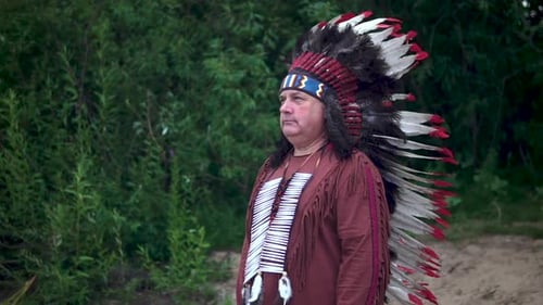 Old Native American Indians Greets Raising His Hand. Stands Against the Background of the Forest