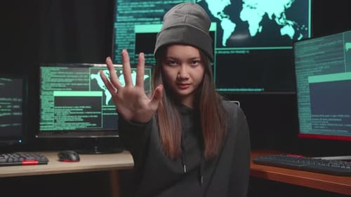 Young Asian Woman Hacker Showing Stop Hand, Code On Multiple Computer Screens