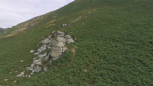 Forward tracking low aerial above green bracken moorland above a rocky stack . Valley of rocks, Exmo